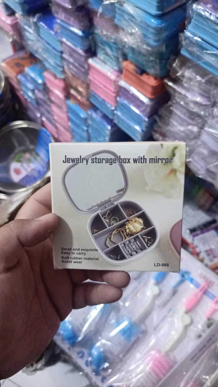 Hand holding a jewelry storage box with mirror packaging in front of stacked boxes.