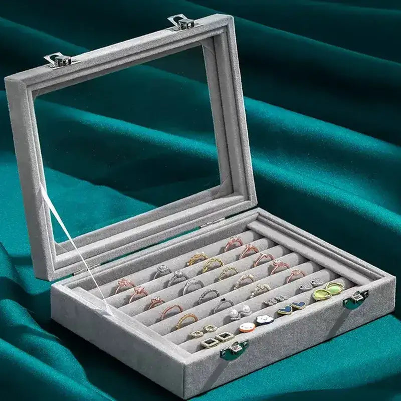 Gray jewelry display box with rings and earrings on a teal fabric background