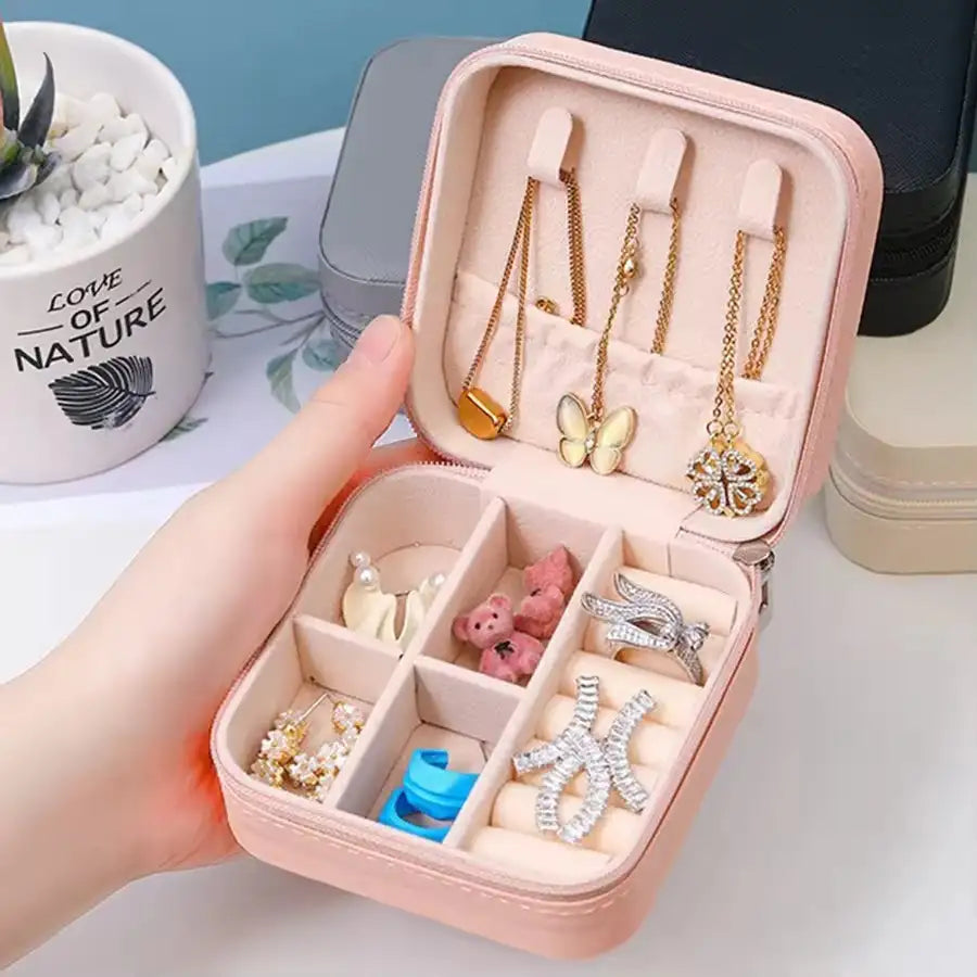 Pink jewelry case with necklaces and other accessories held by a hand, with a 'Love of Nature' mug in the background.