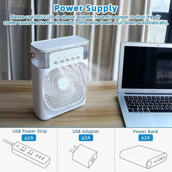 Small air cooler on a table next to a laptop with power supply instructions.